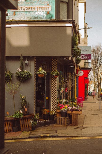 A charming flower shop on St Johns Wood High Street, featuring an inviting display of vibrant floral arrangements and potted plants arranged on wooden crates and hanging baskets outside the storefront
